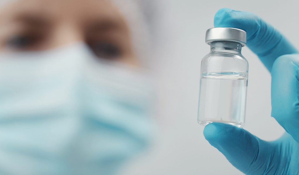 Doctor holding medical vial Cropped shot of doctor holding transparent glass medical vial in hand, focus on bottle